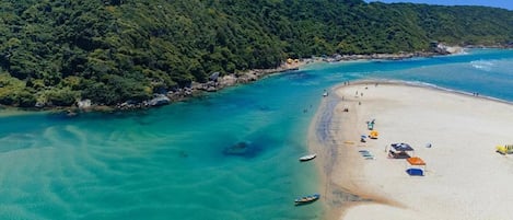 A beach with clear turquoise waters, a sandy shore, and a lush green mountain in the background.