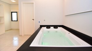 Un baño moderno con una bañera grande, una puerta que conduce a otra habitación y piso de baldosas.
