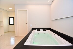 Ein modernes Badezimmer mit einer großen Badewanne, einer Tür zu einem anderen Raum und einem gefliesten Boden.