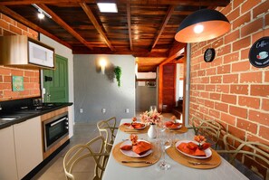 Ein Essbereich mit Backsteinwand, Holzbalkendecke und einem Tisch, gedeckt für vier Personen, mit orangefarbenen Servietten und einem Blumenstrauß.