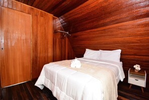 A wooden-paneled room with a bed, a nightstand, and a small table with a vase.