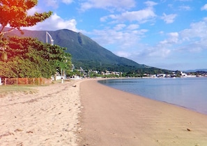 A beach with a mountain in the background, a clear sky, and a fence along the shore.