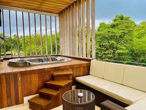 Ein Whirlpool mit Holzstufen und einer Sitzecke, umgeben von einer Holzterrasse und großen Fenstern.
