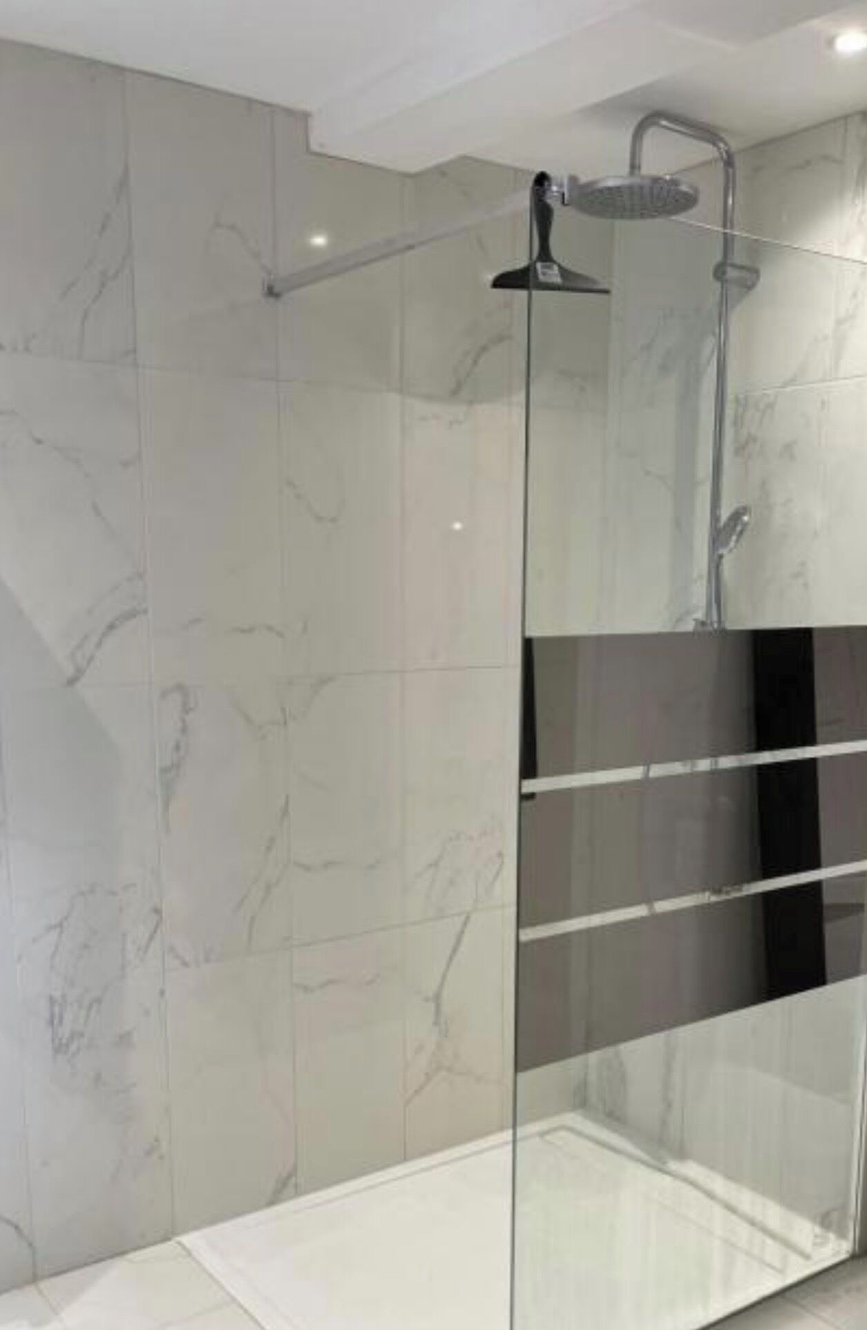 Une douche moderne avec une porte en verre, des murs en marbre et un pommeau de douche apparent.