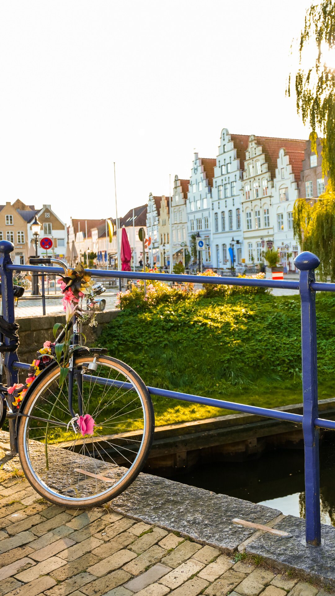 Un vélo décoré de fleurs, un canal et, au fond, des bâtiments historiques.
