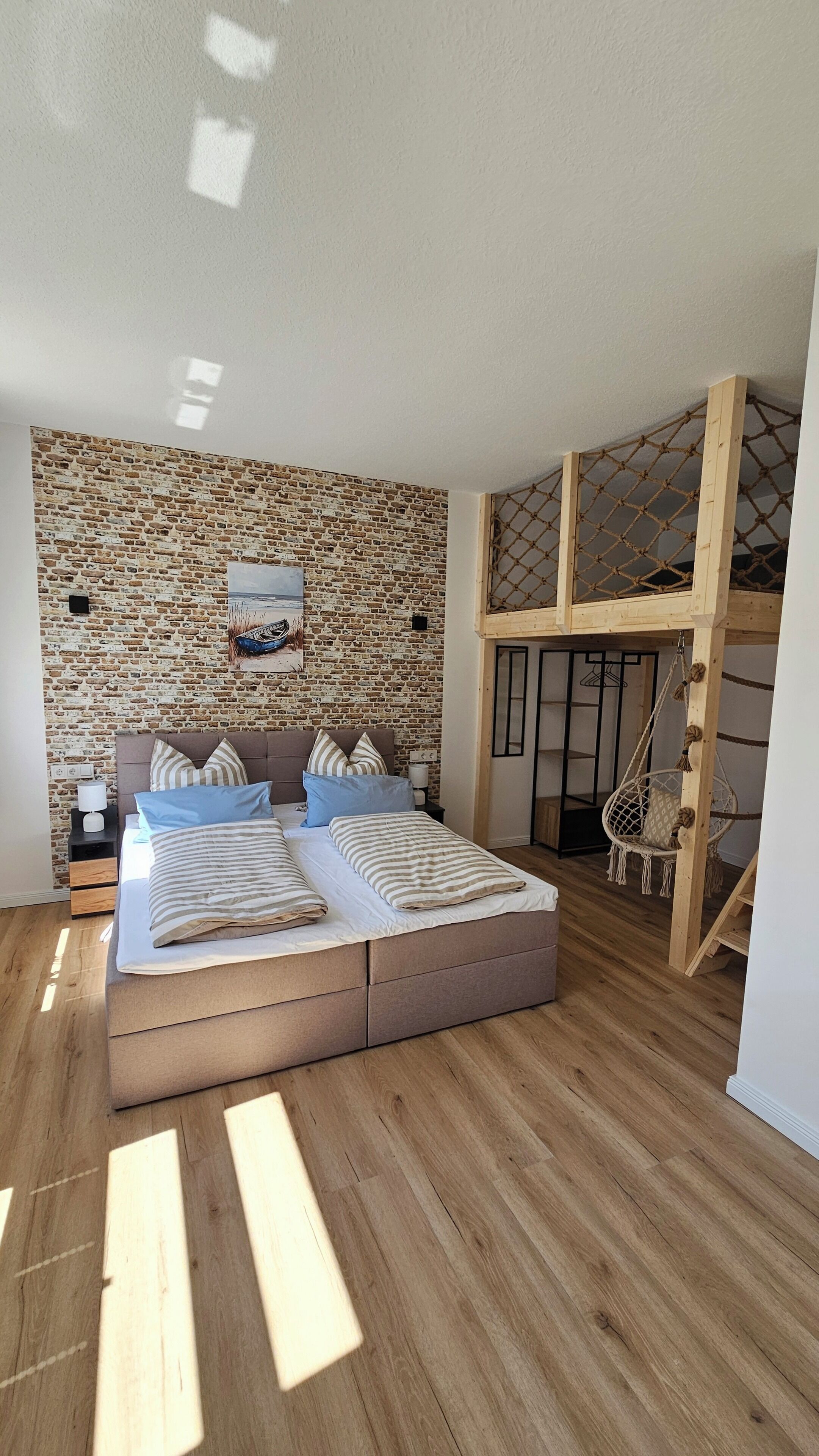 Ein Schlafzimmer mit Backsteinwand, einem Bett mit gestreifter Bettwäsche, Holzboden und einer Hängeschaukel.