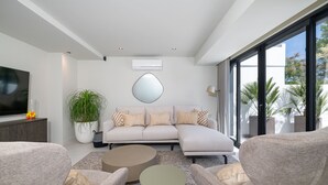 A modern living room with a sectional sofa, two armchairs, a coffee table, a large mirror, and a television on a stand. - Prestige Luxury Marina (Loulé)