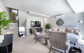 Ein modernes Wohnzimmer mit einer Couch, Sesseln, einem Fernseher und einer Treppe.