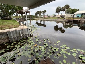 A calm water body with lily pads, a wooden dock, and a covered walkway. - Quiet and Cozy Waterfront rental; with dock to Lock access into Lake Okeechobee (Okeechobee)