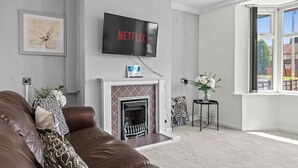 Una sala de estar con un sofá de cuero marrón, chimenea, televisor montado y ventanal con vistas.