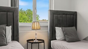 Habitación con dos camas, una lámpara y ventana con vistas a zonas verdes.