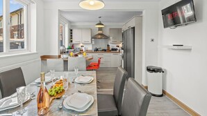 Una cocina moderna con armarios blancos, un comedor con mesa para cuatro y un televisor montado en la pared.