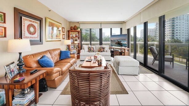 A spacious living room with a leather sofa, a white armchair, a coffee table, and a large window offering a city view. - Unit for RENT in Miami, Aventura area. Six months MINIMUM. (Miami)