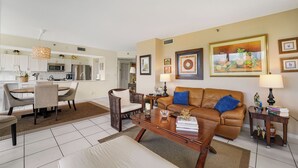 A living room with a brown leather sofa, a wooden coffee table, a dining area with a round table and chairs, and a kitchen in the background. - Unit for RENT in Miami, Aventura area. Six months MINIMUM. (Miami)