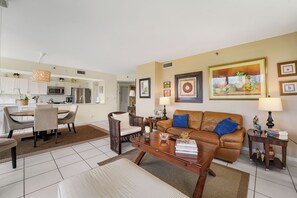 Ein Wohnzimmer mit braunem Ledersofa, einem Holztisch, einer Essecke mit rundem Tisch und Stühlen sowie einer Küche im Hintergrund.