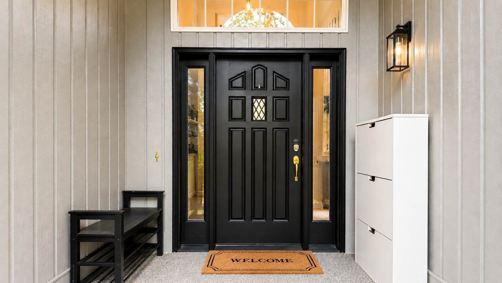 Une porte noire avec un paillasson, une petite table et un meuble blanc.