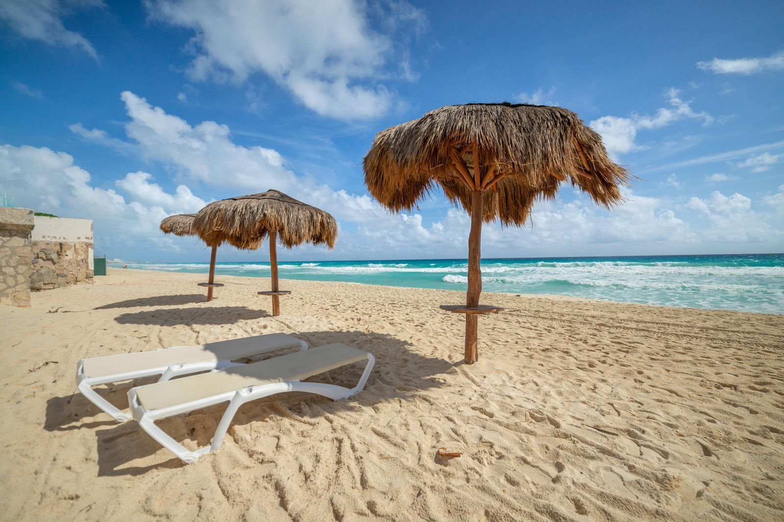 A beach with thatched umbrellas and a white lounge chair.
