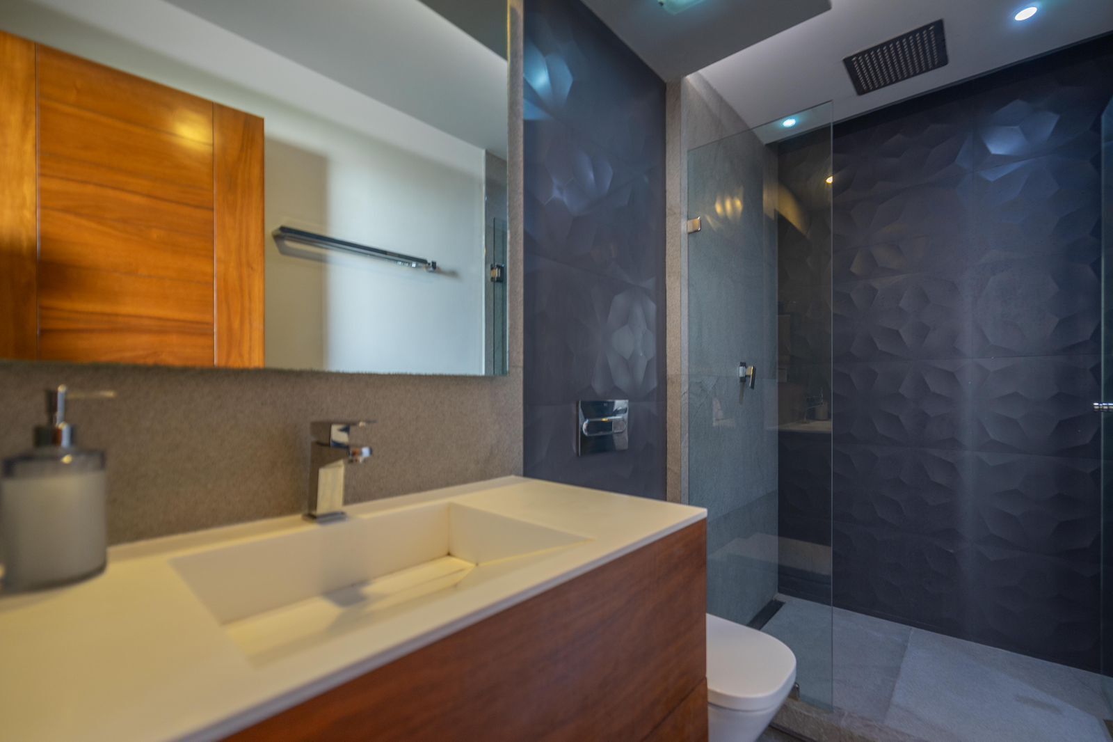 A modern bathroom with a wooden vanity, a large mirror, a shower enclosure, and a toilet.