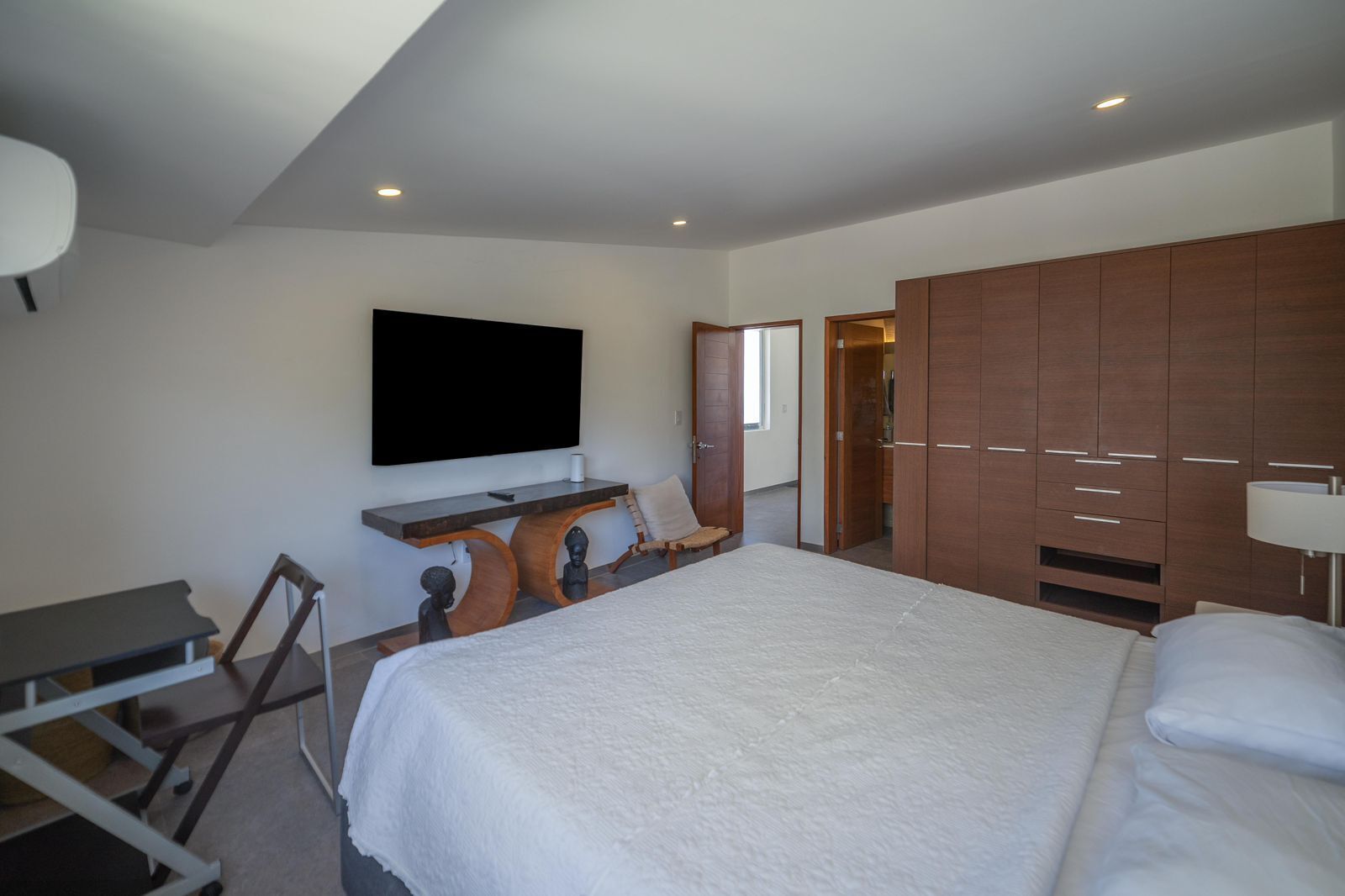 Un dormitorio moderno con una cama grande, un televisor montado en la pared, un armario de madera y un escritorio con una silla.