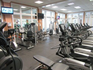 Une salle de sport équipée de divers appareils d’exercice, de miroirs et d’un écran de télévision.