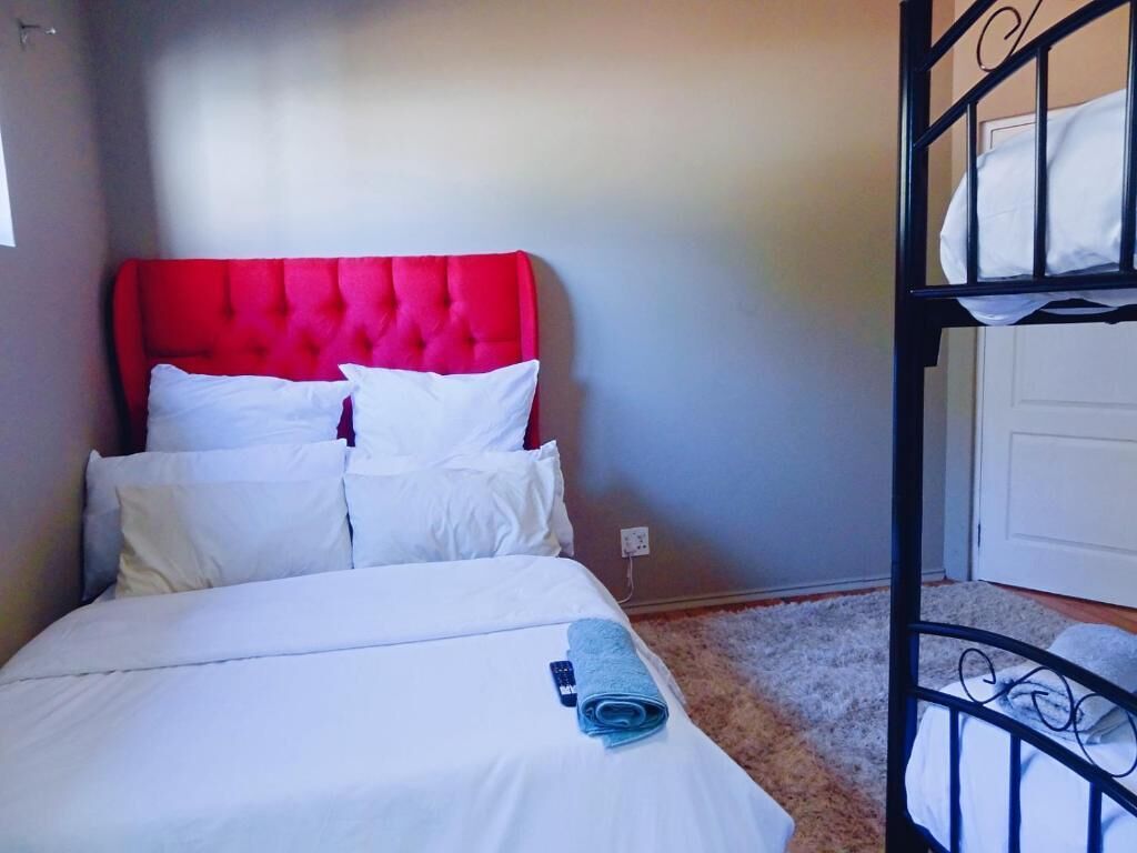 A room with a bed featuring a red headboard, white bedding, and a rolled towel.