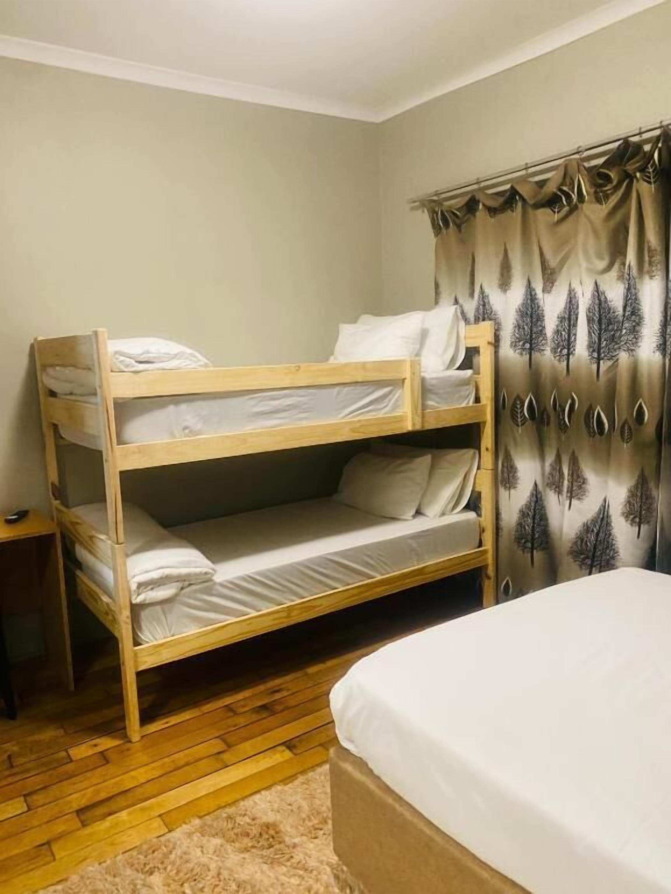 A bunk bed in a room with a wooden floor, a small bedside table, and a curtain with a tree pattern.