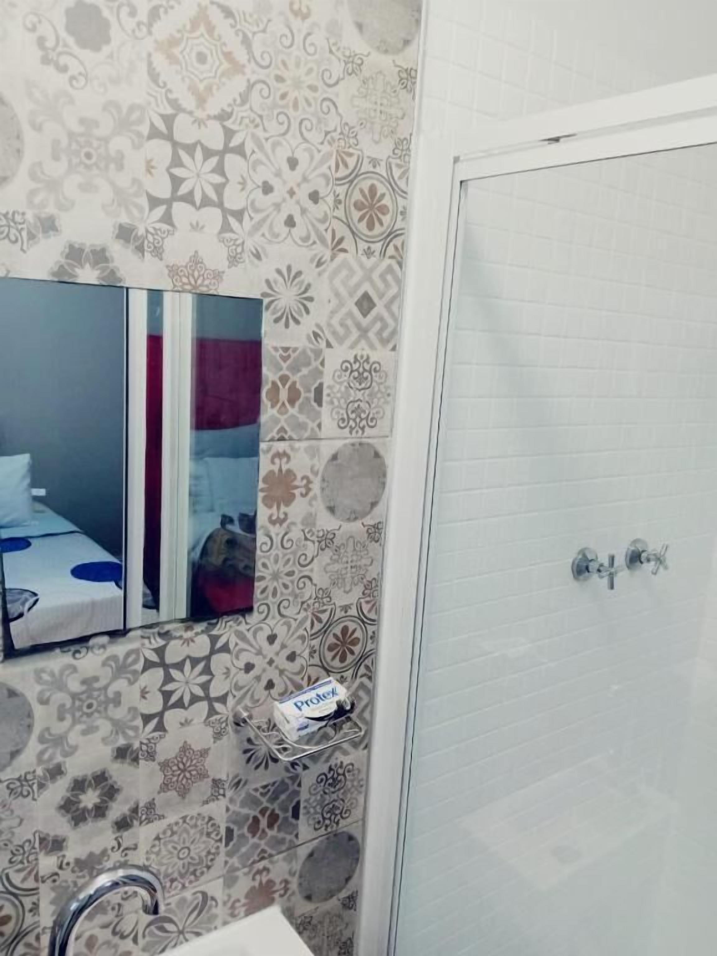 A bathroom with patterned tiles, a mirror, a sink, and a shower area.