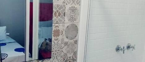 A bathroom with patterned tiles, a mirror, a sink, and a shower area.
