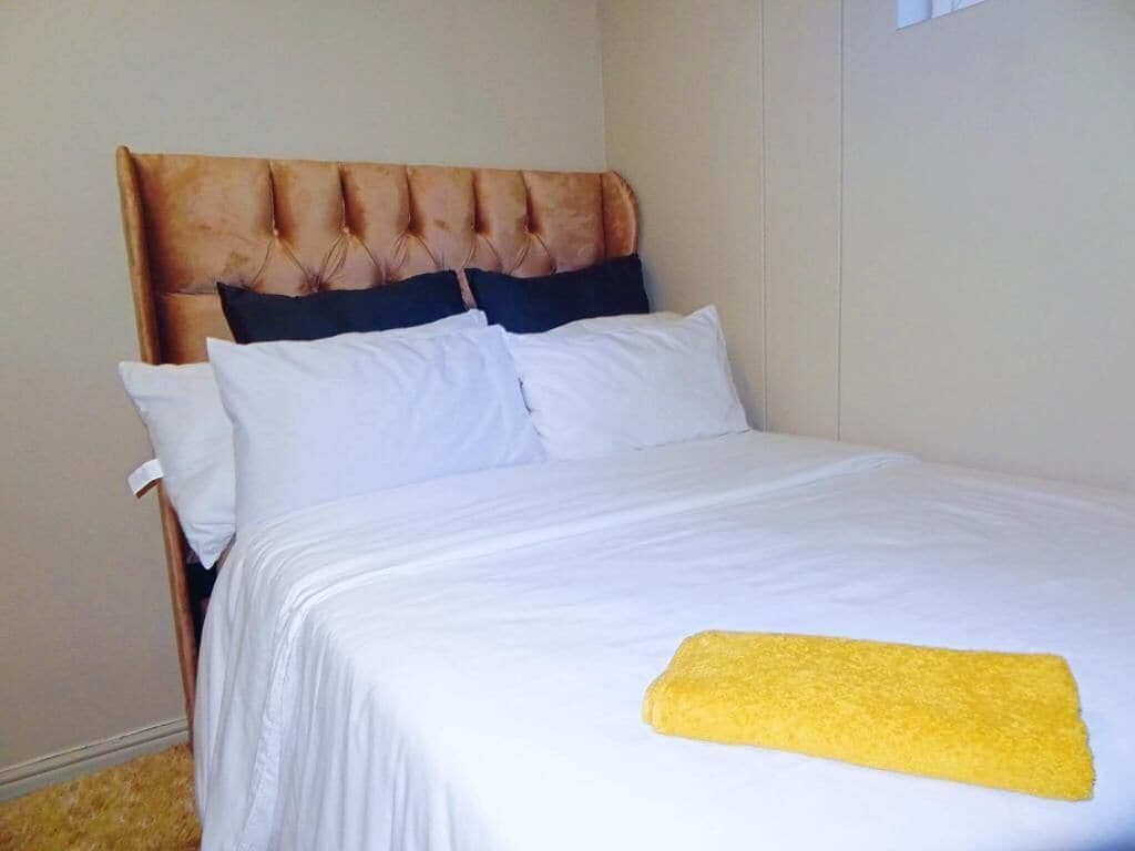 A bed with a tufted headboard, white bedding, and a yellow towel.