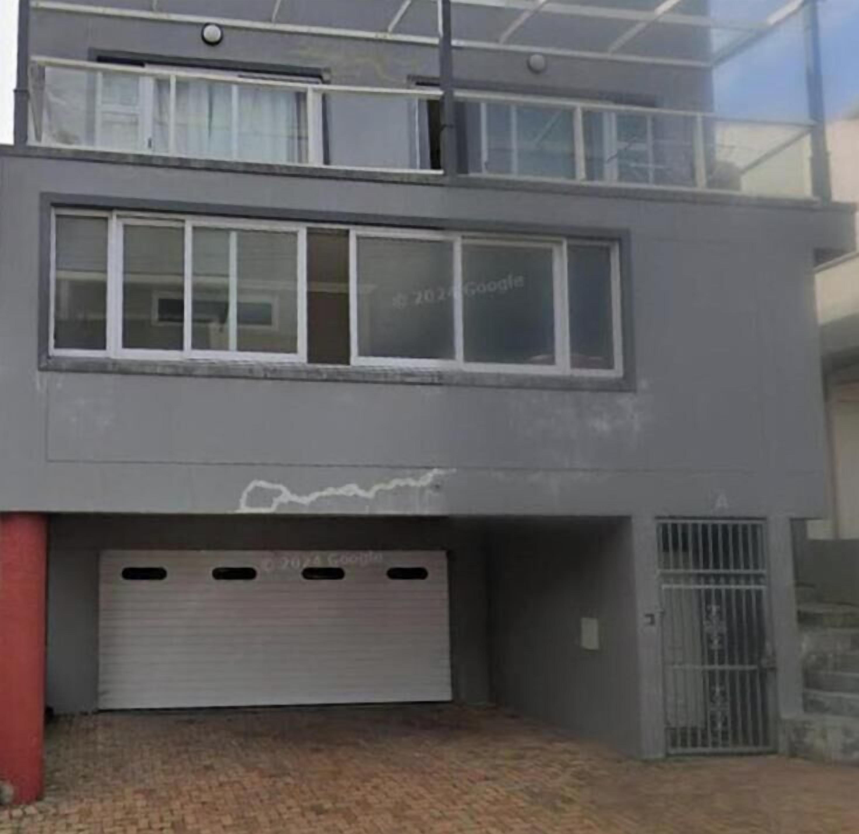 Un edificio de dos pisos con puerta de garaje, ventanas y una reja metálica.