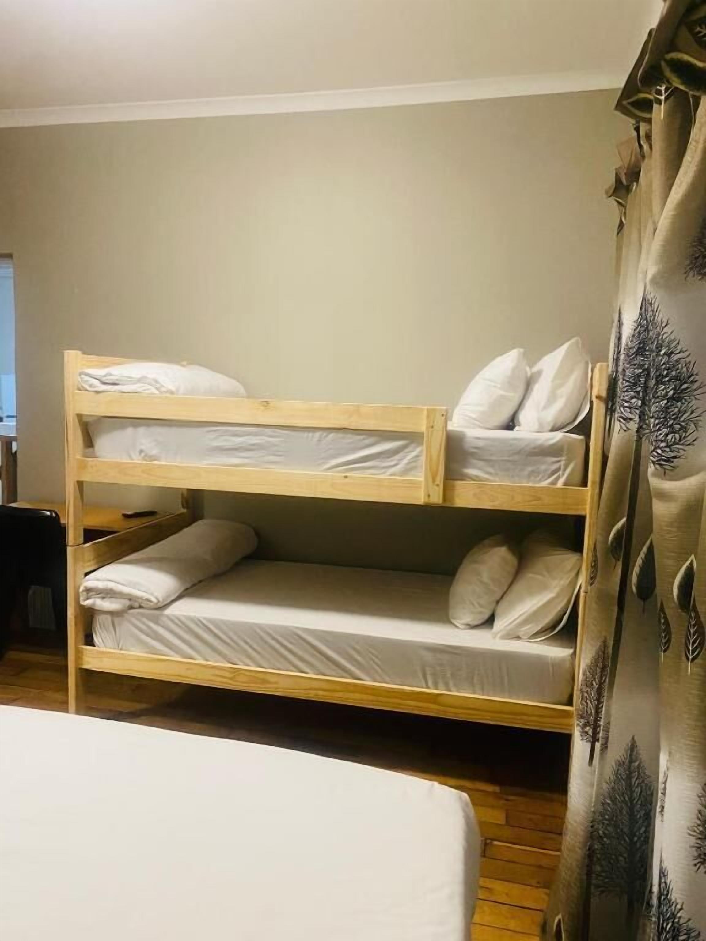 A bunk bed with two levels, a curtain with a leaf pattern, and a window in the background.