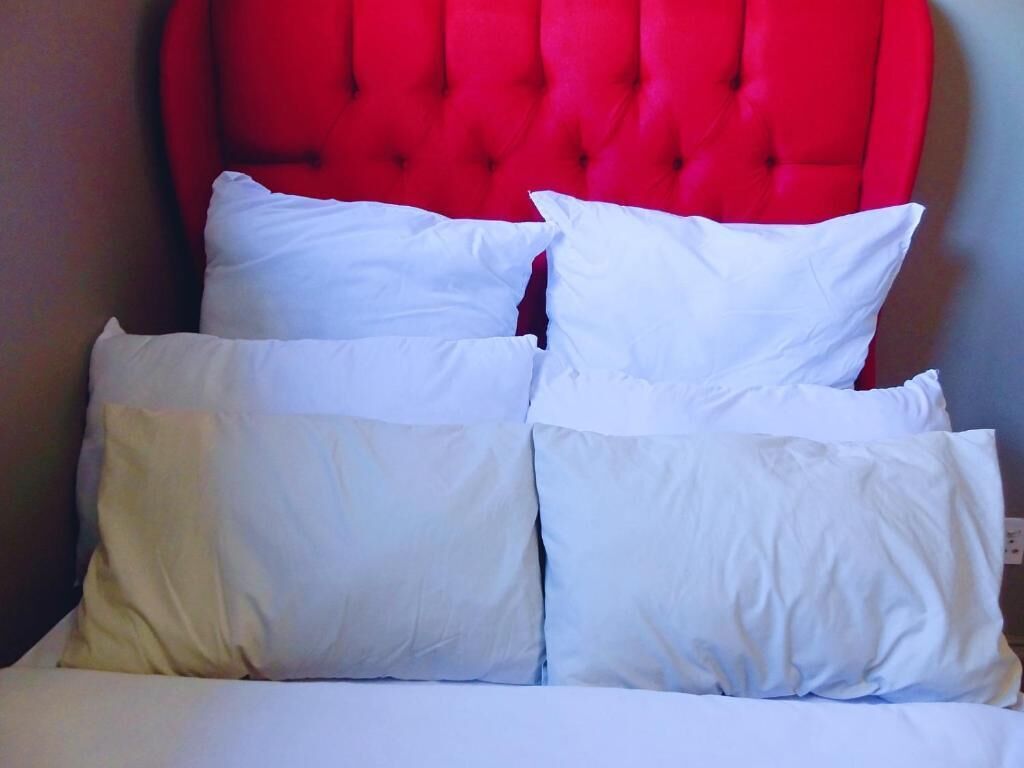 Een bed met witte lakens en een rode bekleden hoofdeinde.