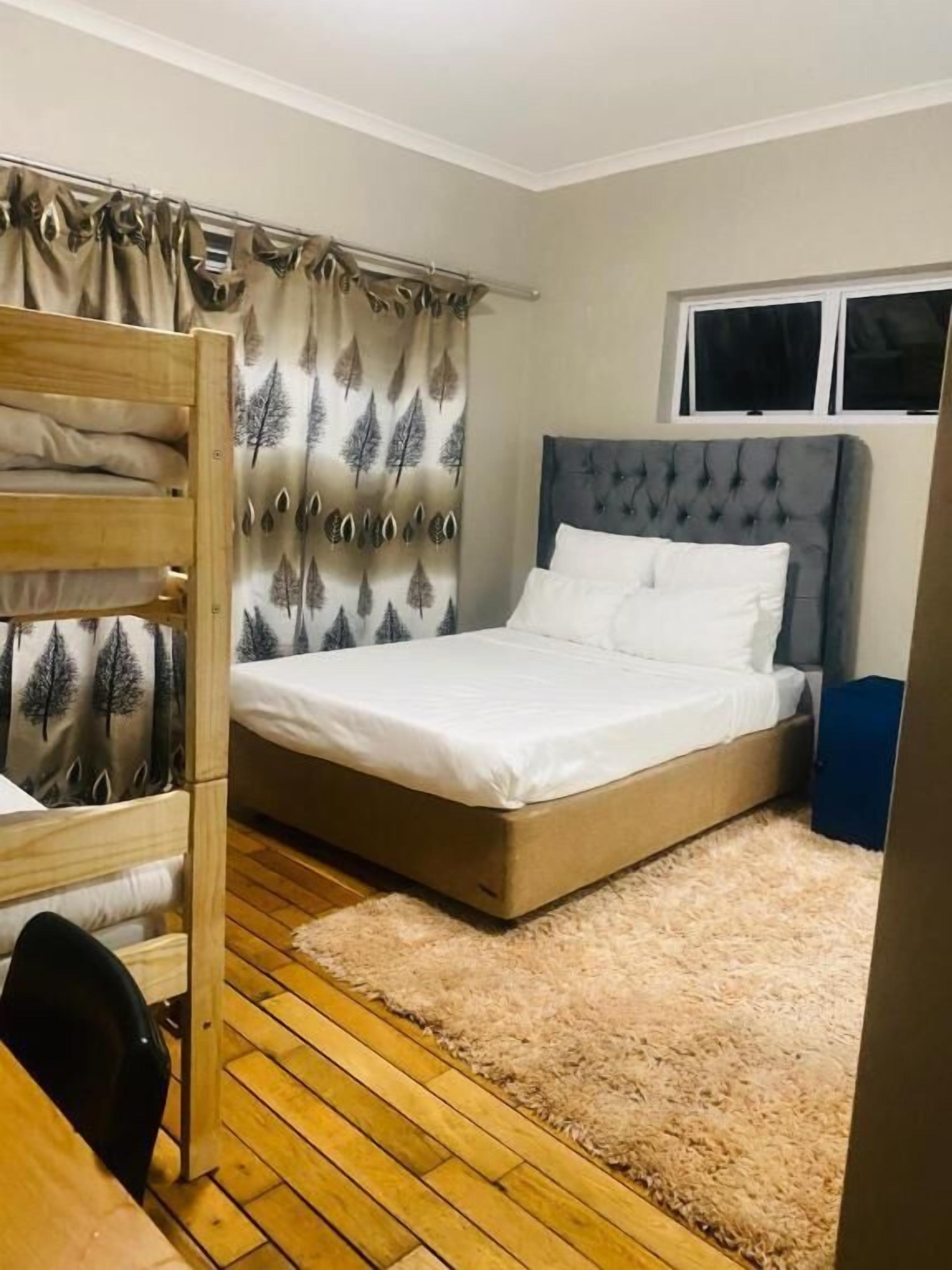 A bedroom with a bed, a wooden bunk bed, a window, and a curtain with a tree pattern.