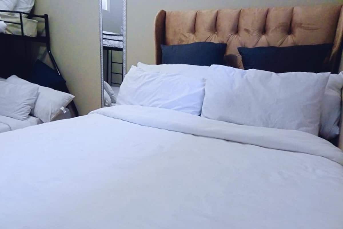 Una cama con ropa blanca, cabecera con diseño capitonado y una vista parcial de una mesita de noche con lámpara.