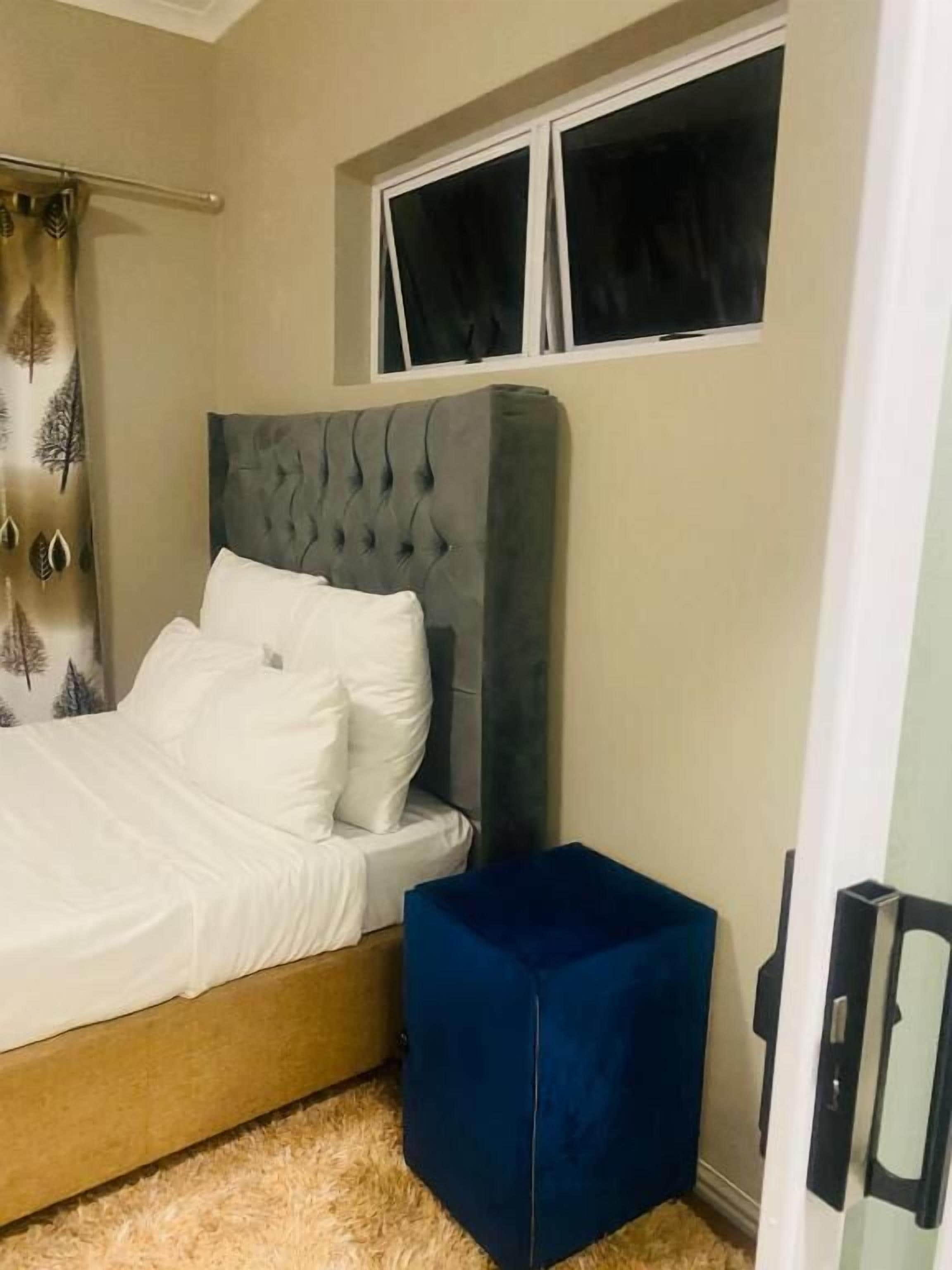 Ein Schlafzimmer mit einem Bett, einem Fenster und einem blauen Hocker.