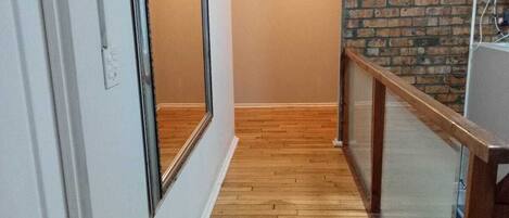 Un couloir avec un plancher en bois, des murs blancs, un miroir et un mur d’accent en briques.