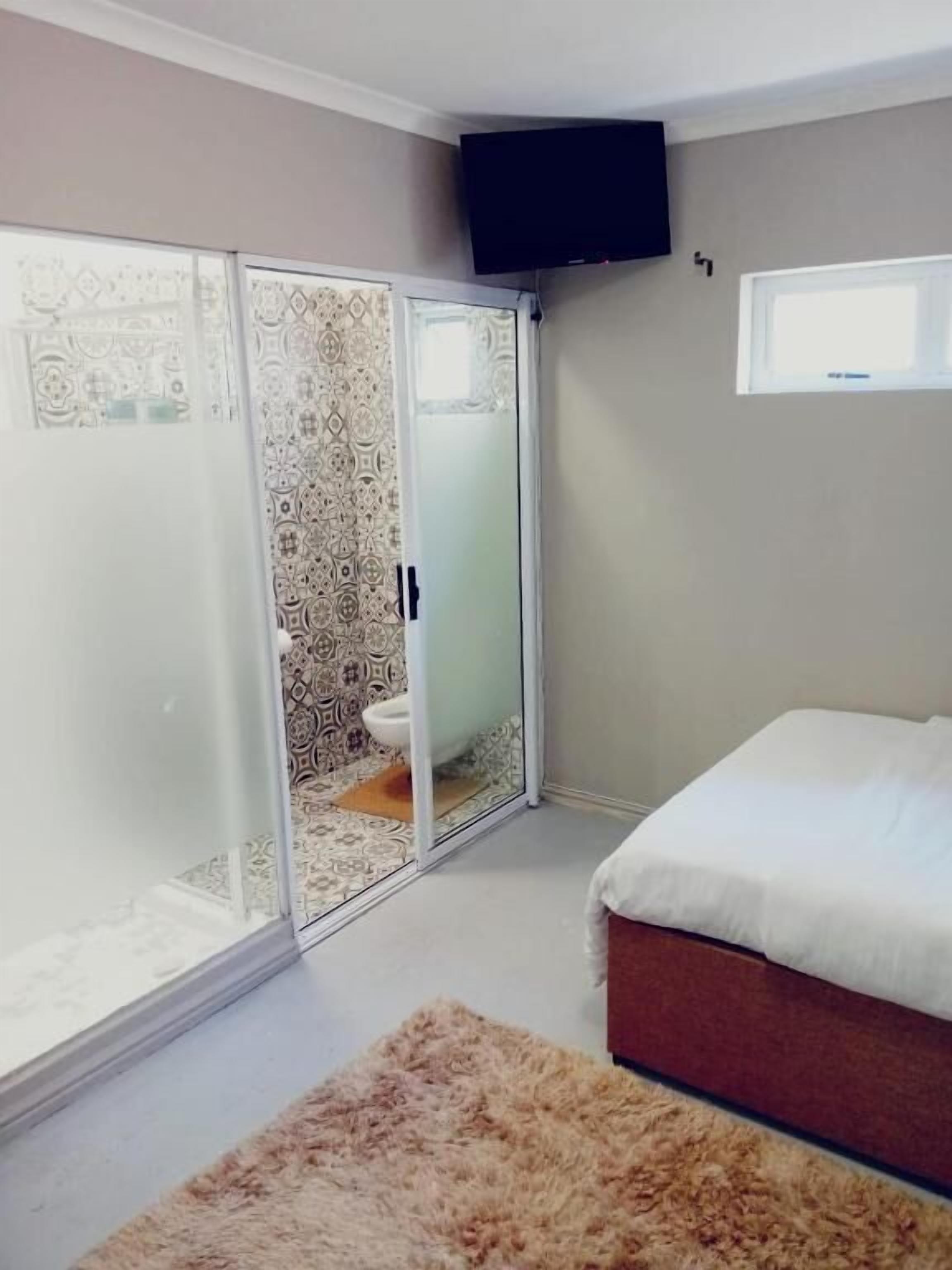 Une chambre à coucher avec un lit, une porte-fenêtre coulissante donnant sur une salle de bain, un téléviseur fixé au mur et une fenêtre.