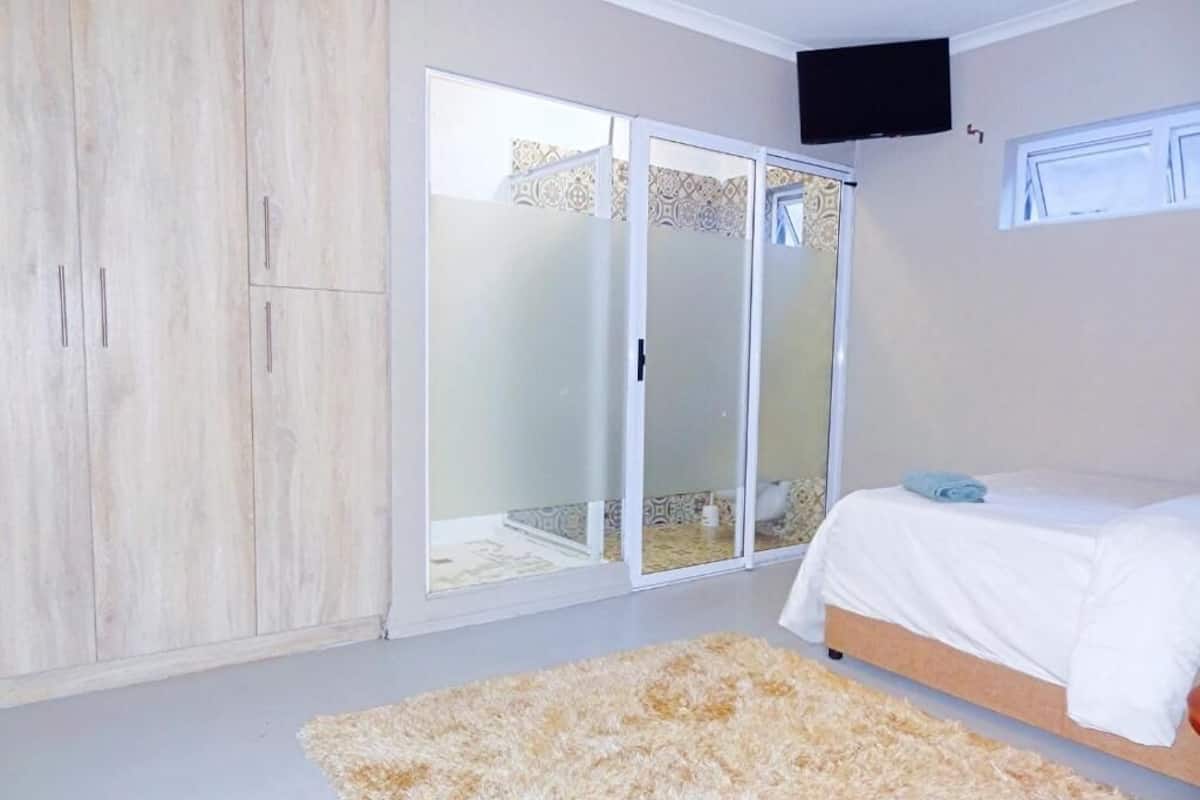 Un dormitorio con cama, armario, puerta corredera de vidrio y televisor en la pared.
