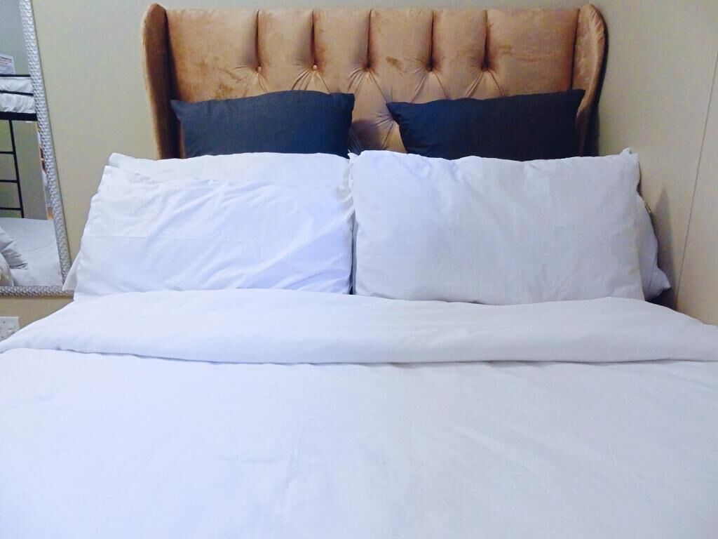 A bed with a tufted headboard, two white pillows, and a white bedspread.