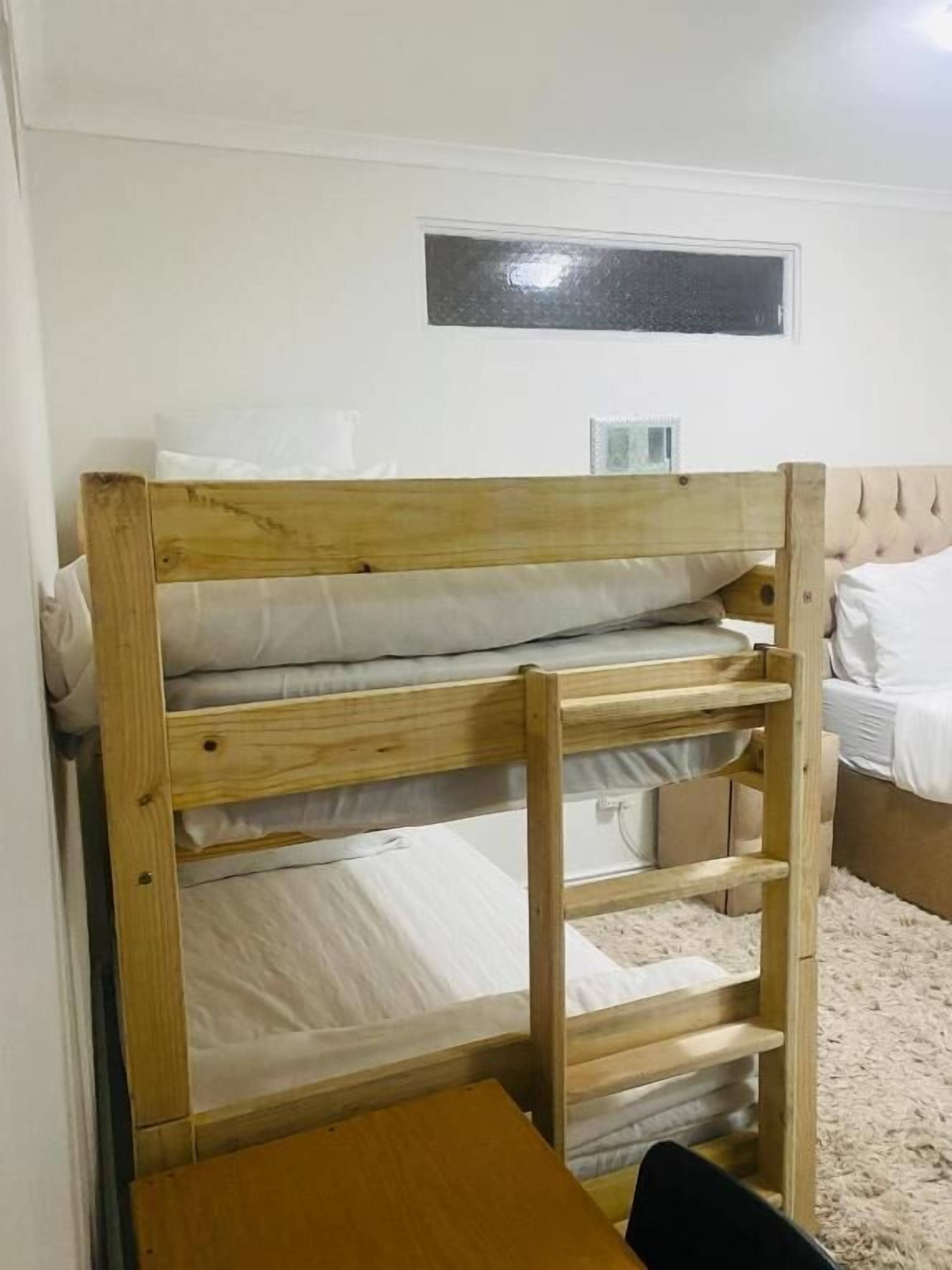 Een stapelbed met houten frame, een klein tafeltje en een raam met metalen frame.
