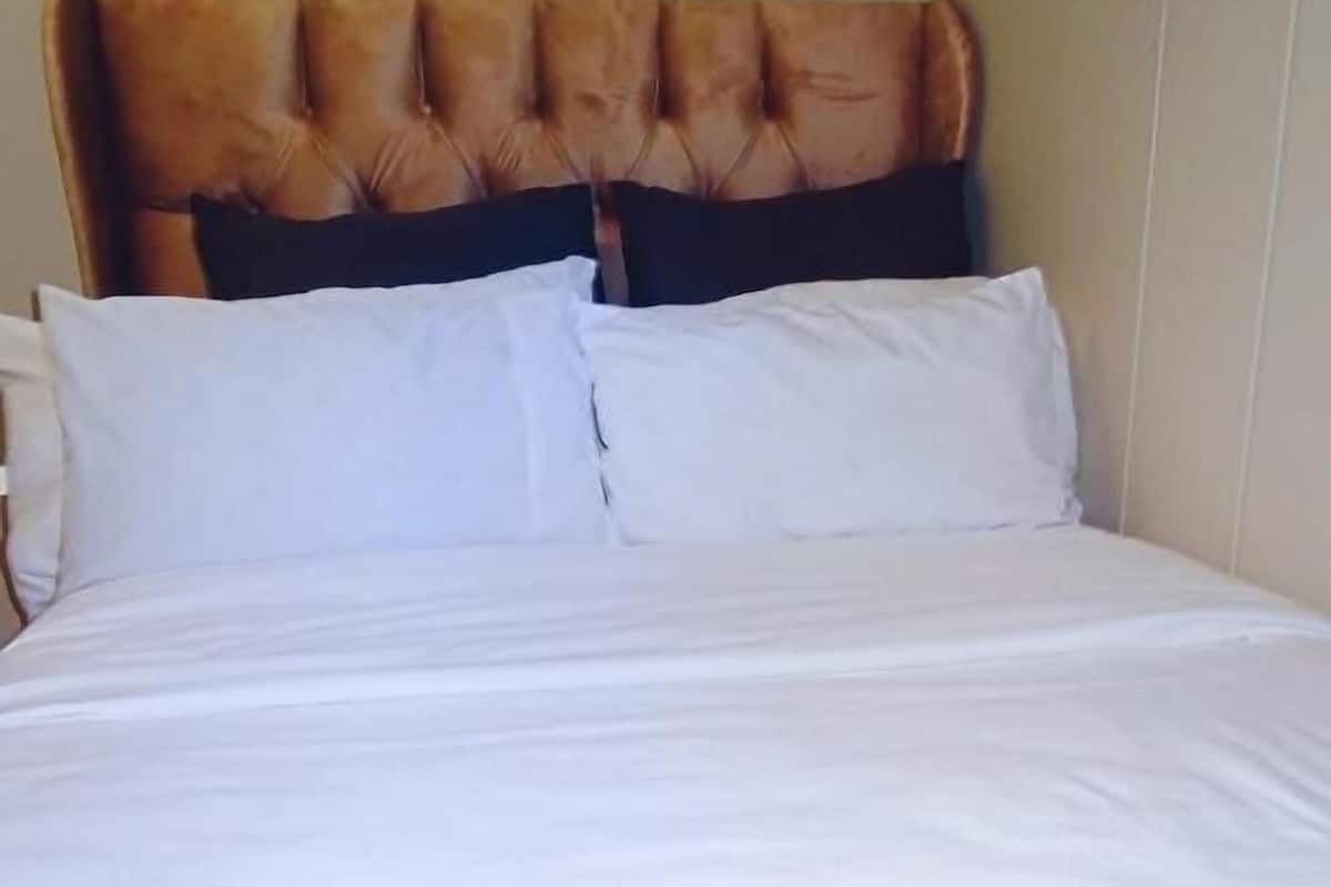 Una cama con cabecera capitonada, dos almohadas blancas y un plaid amarillo.