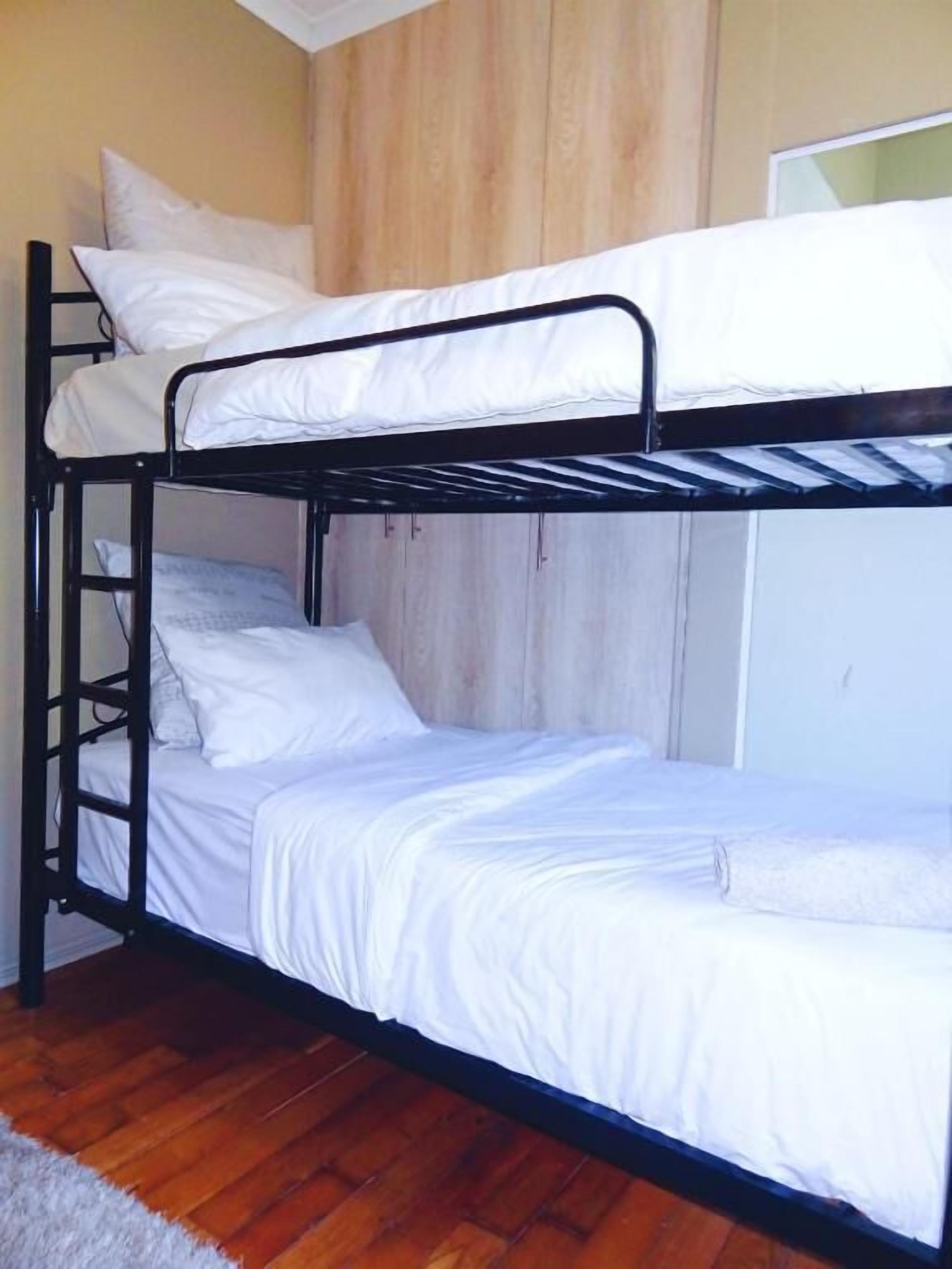 Een stapelbed met witte beddengoed in een kamer met houten vloeren en een witte deur.