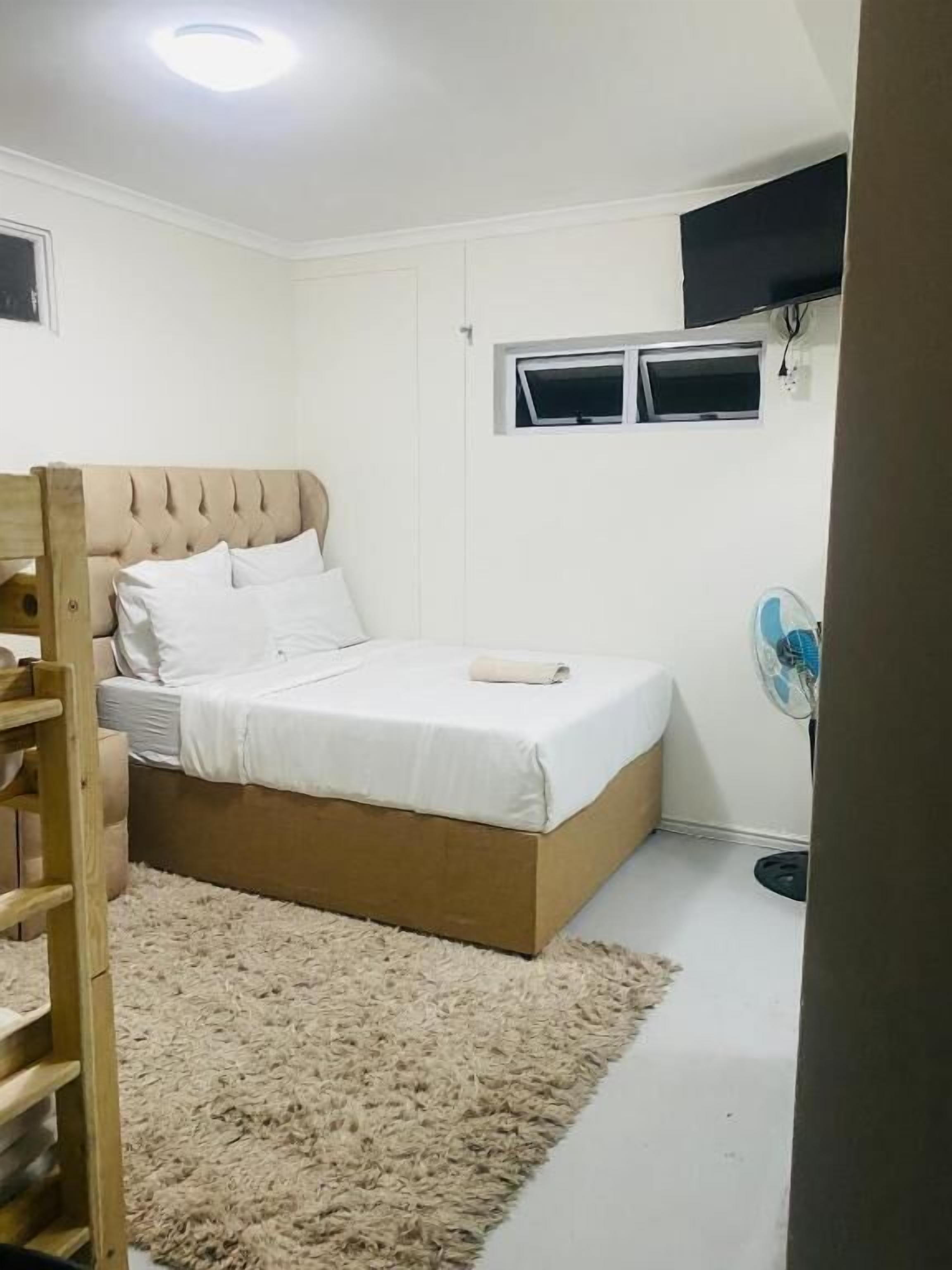 A bedroom with a bed, a wooden ladder, a small window, and a wall-mounted fan.