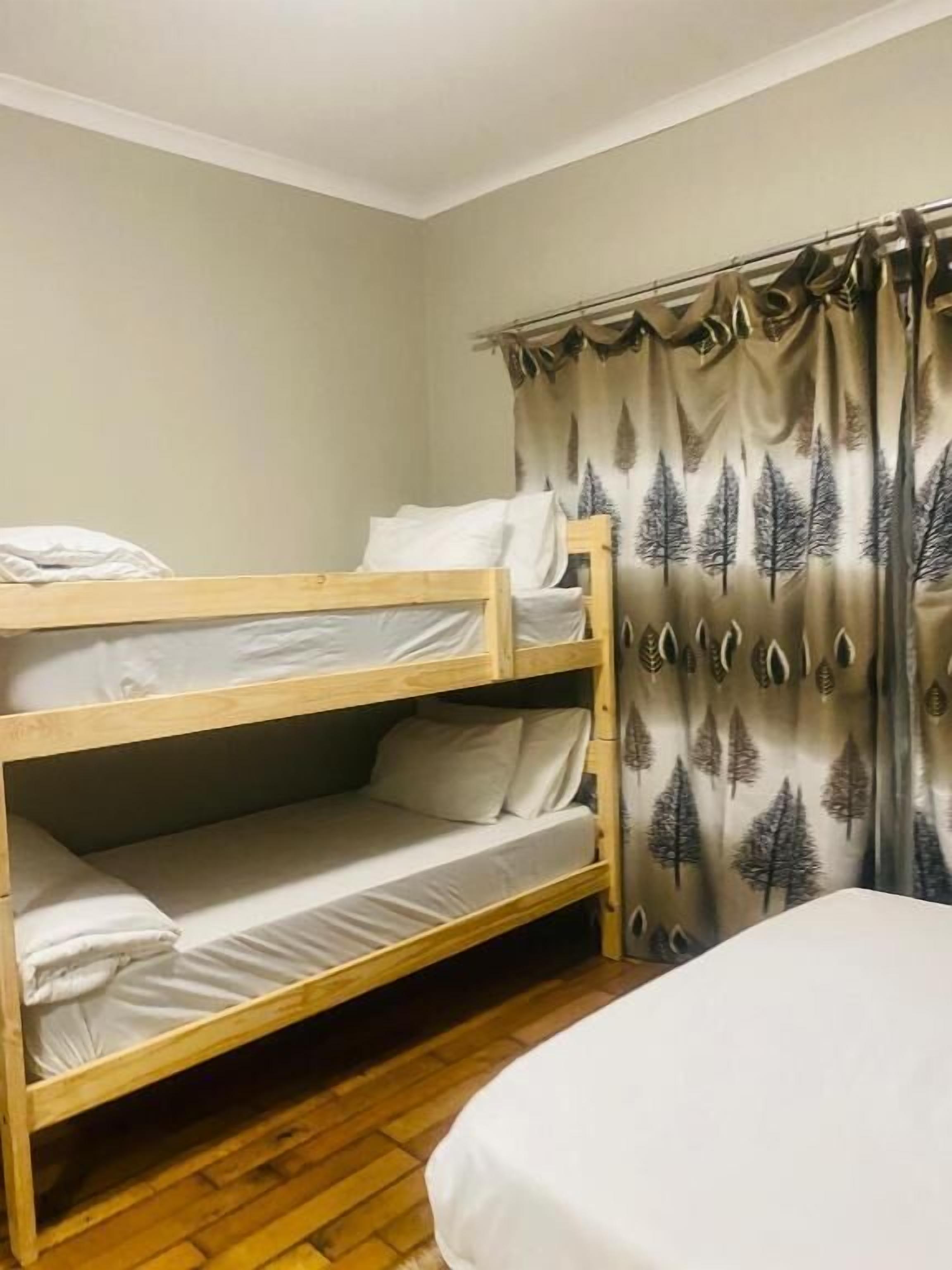 A bunk bed room with a curtain featuring a tree pattern, a wooden floor, and a bed with white bedding.