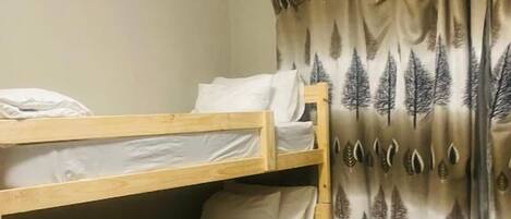 A bunk bed room with a curtain featuring a tree pattern, a wooden floor, and a bed with white bedding.