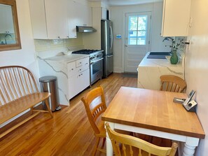 A kitchen with white cabinets, a stainless steel refrigerator, a stove, and a wooden dining table with chairs.