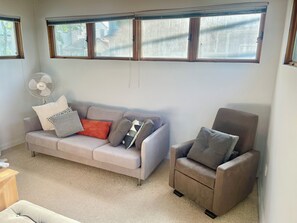 Un salón con sofá, sillón y un ventilador de pie.