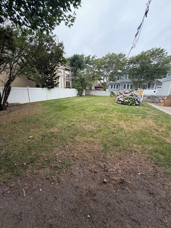 A residential backyard with a lawn, a white fence, and a flower bed.