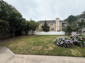 Un patio trasero residencial con césped, cerca blanca y una casa con chimenea.