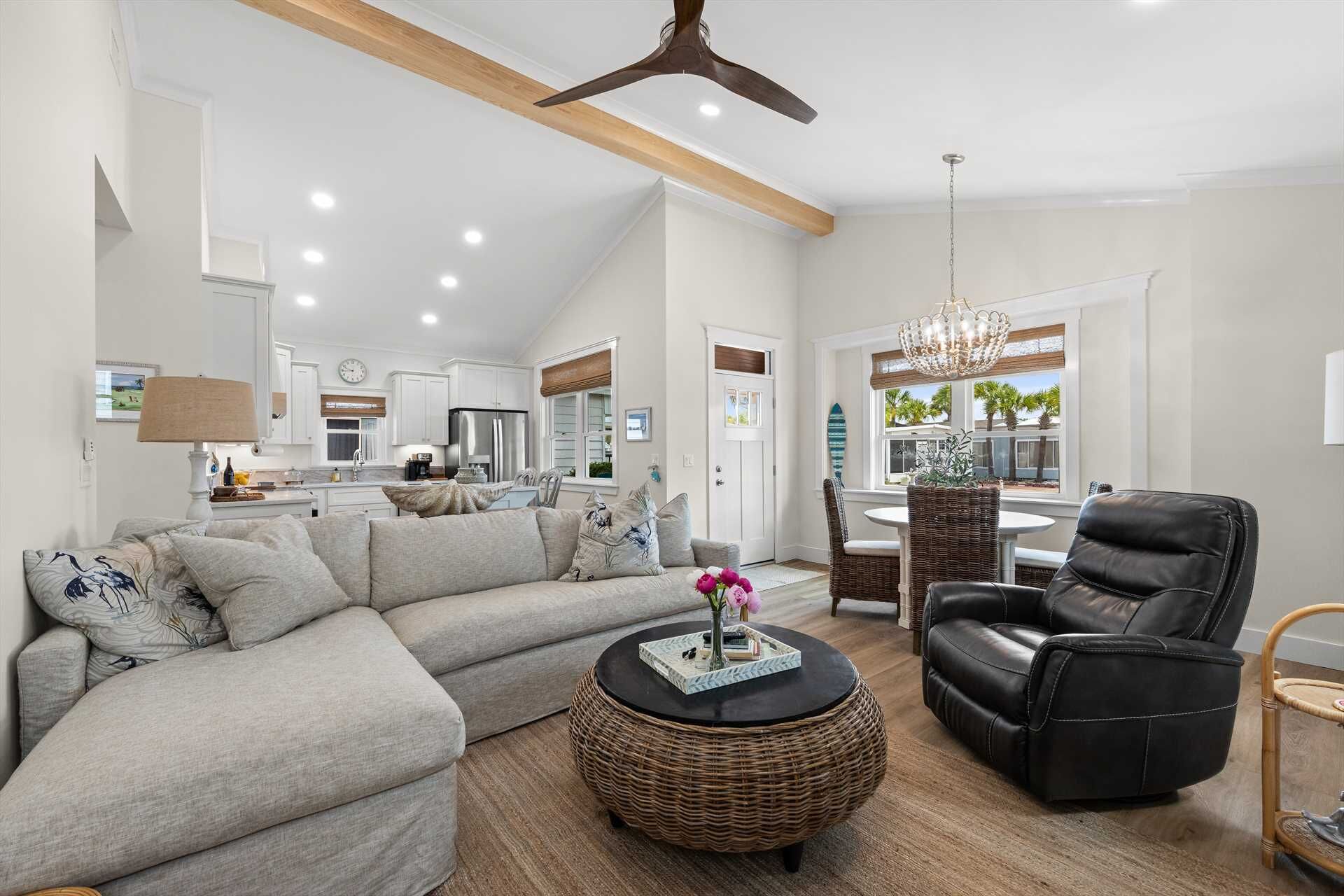 A spacious living room with a sofa, a black leather chair, a round wicker coffee table, and a dining area with a table and chairs.